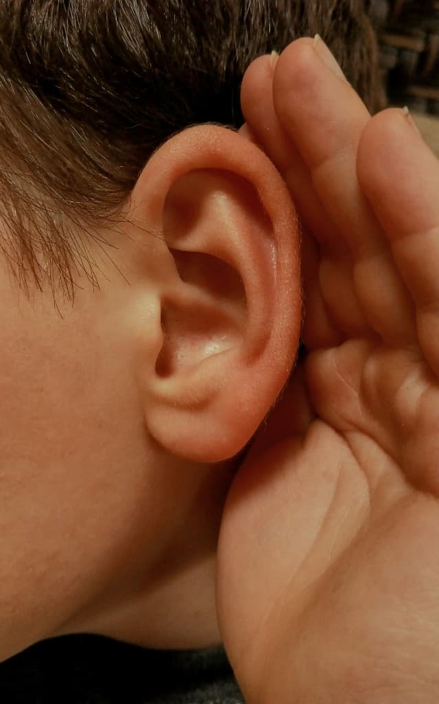 Close-up of a child's ear with a hand cupped behind it, representing hearing health and early screening