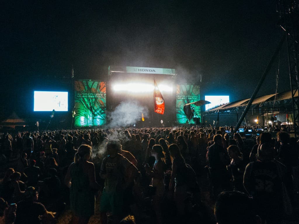 Crowd at an outdoor music festival with stage lights and smoke at night