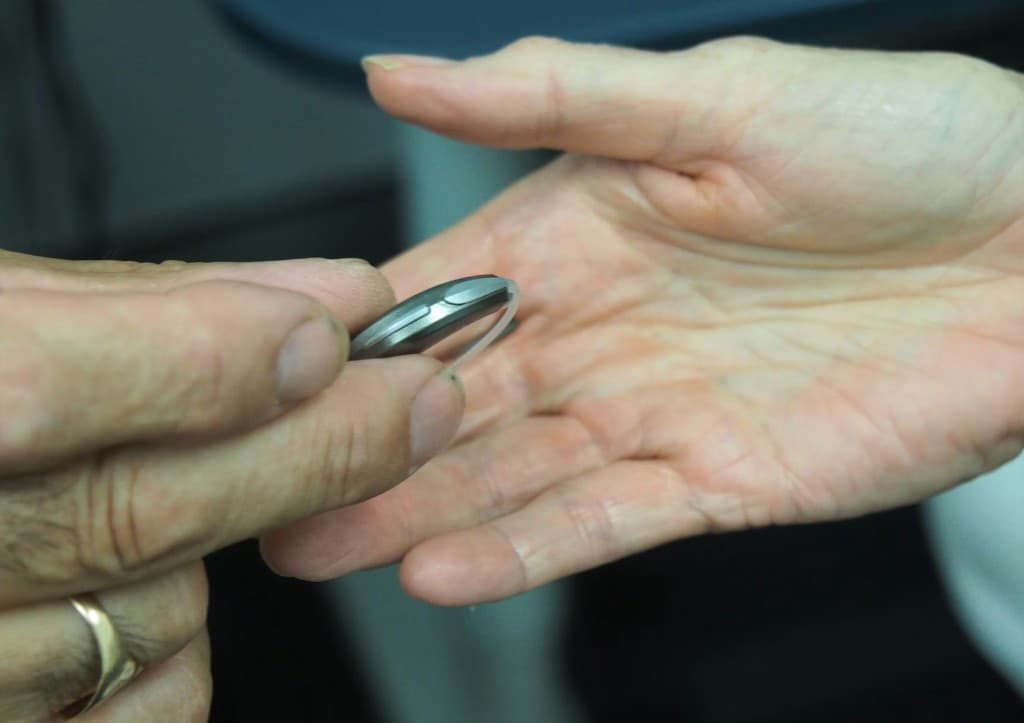 Audiologist holding a behind-the-ear hearing aid in a patient's open palm during a clean-and-check