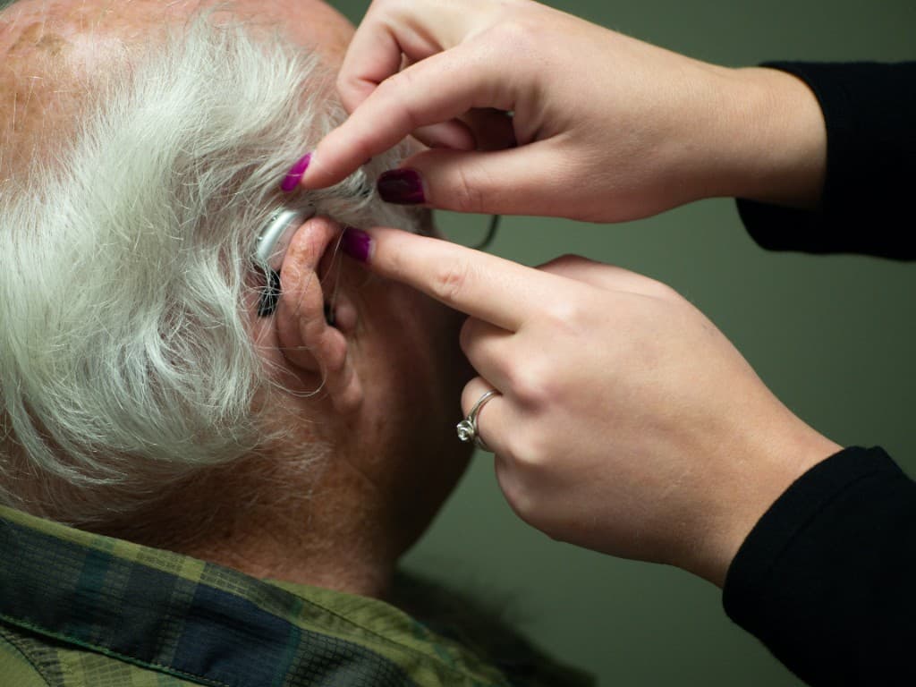 Audiologist fitting a behind-the-ear hearing aid on an elderly patient