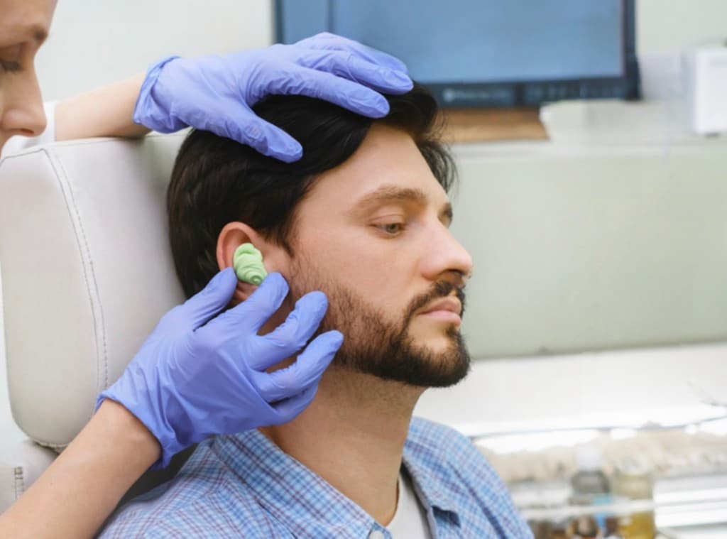 Audiologist taking a custom ear impression with purple silicone material for swim molds